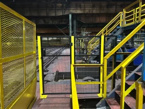 Black and yellow machine guarding door beside steel stairs at a Sheffield site